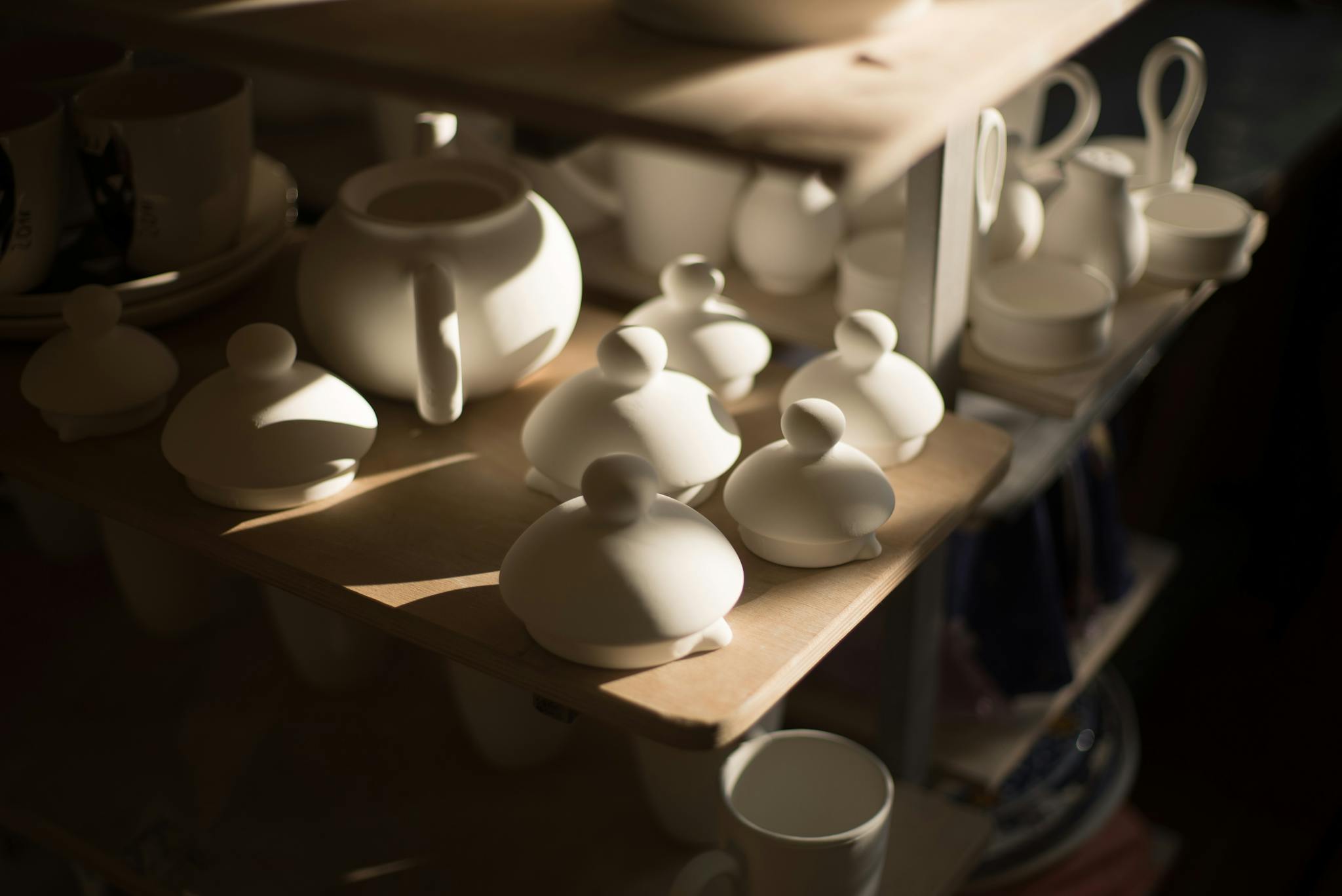 A display of handcrafted ceramic teapots and lids on a wooden shelf, bathed in gentle light.